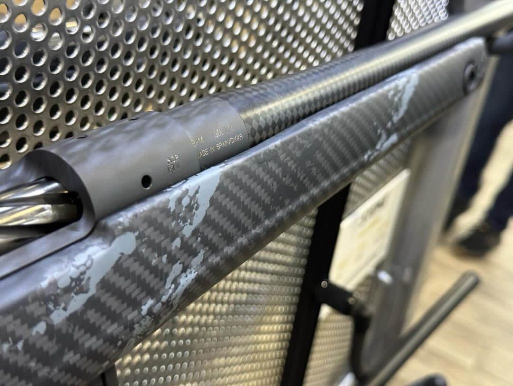 A closeup of the forend and barrel of a rifle shows carbon fiber construction.