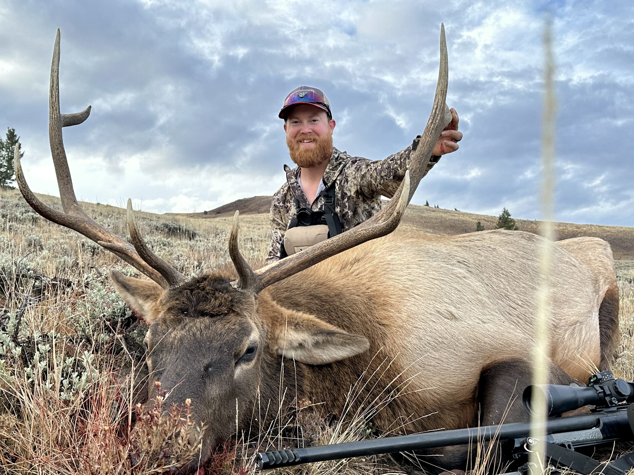 A hunter in camo poses with his bull elk.