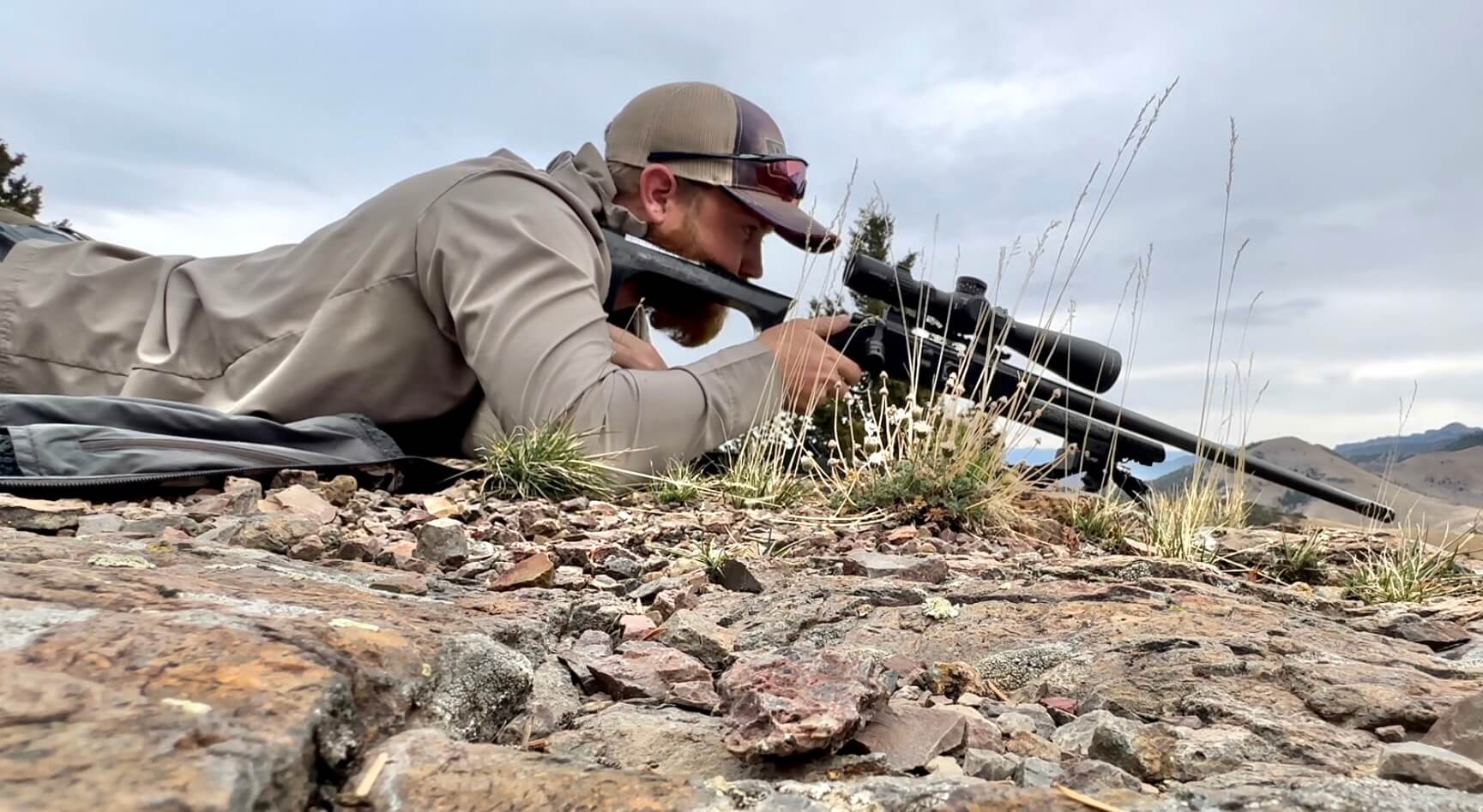 A hunter lays prone behind his long range rifle in preparation for his shot.