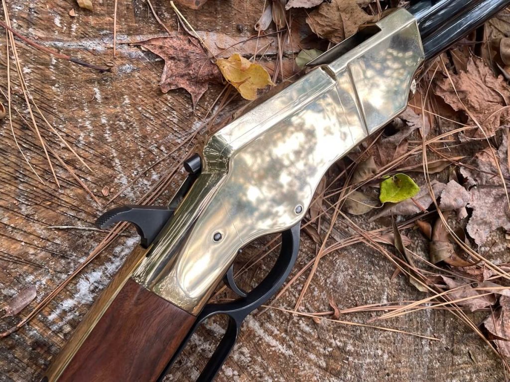 The New Original Henry rifle brass receiver against a backdrop of leaves and pine needles