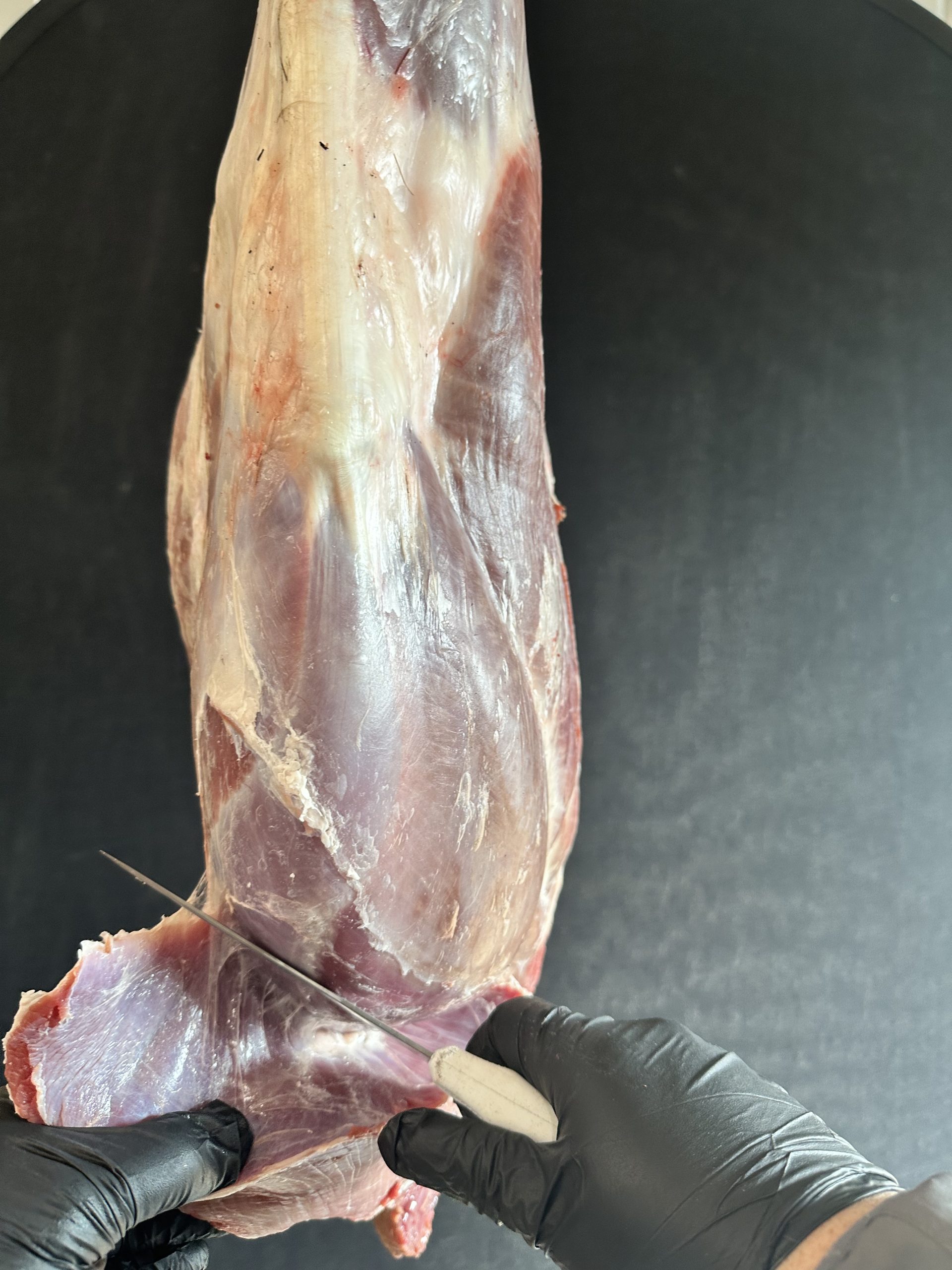 Gloved hands cutting the tri-tip from the sirloin tip