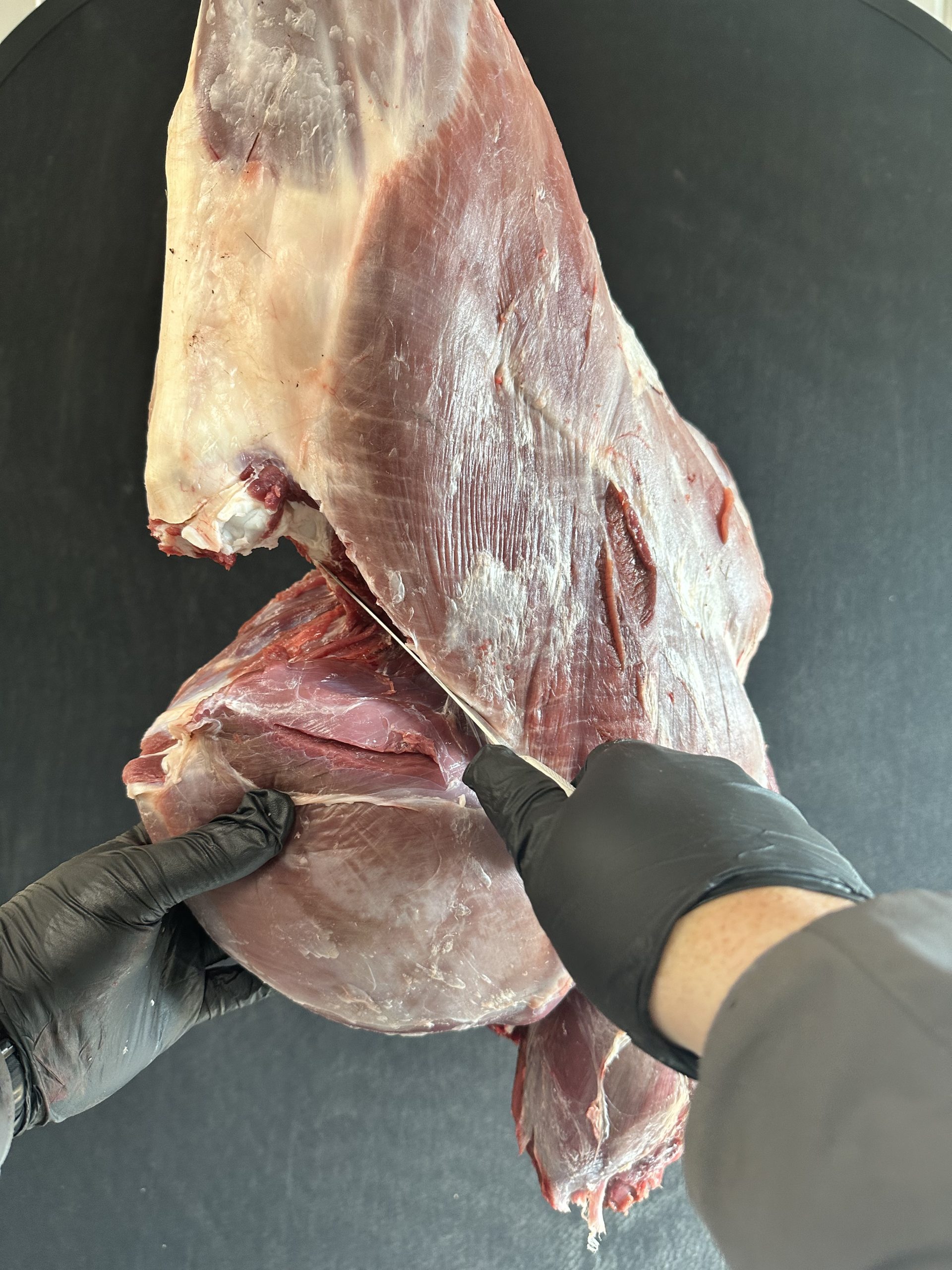 Gloved hands using a knife to deal with the sirloin tip