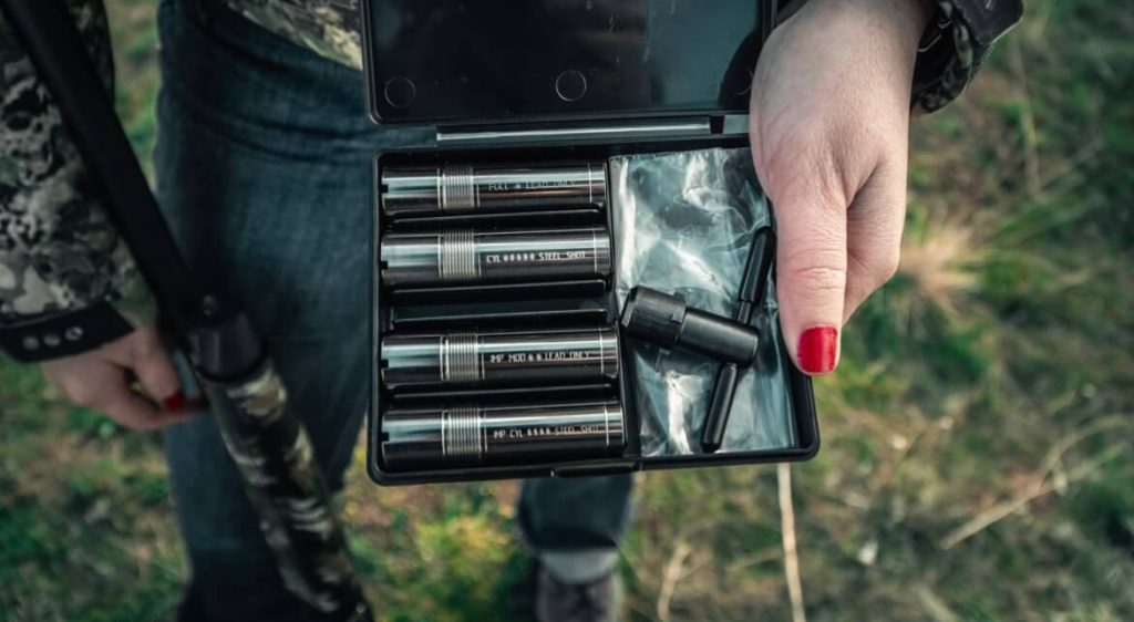 Woman with nail polish and camo jacket holds tools for shotgun