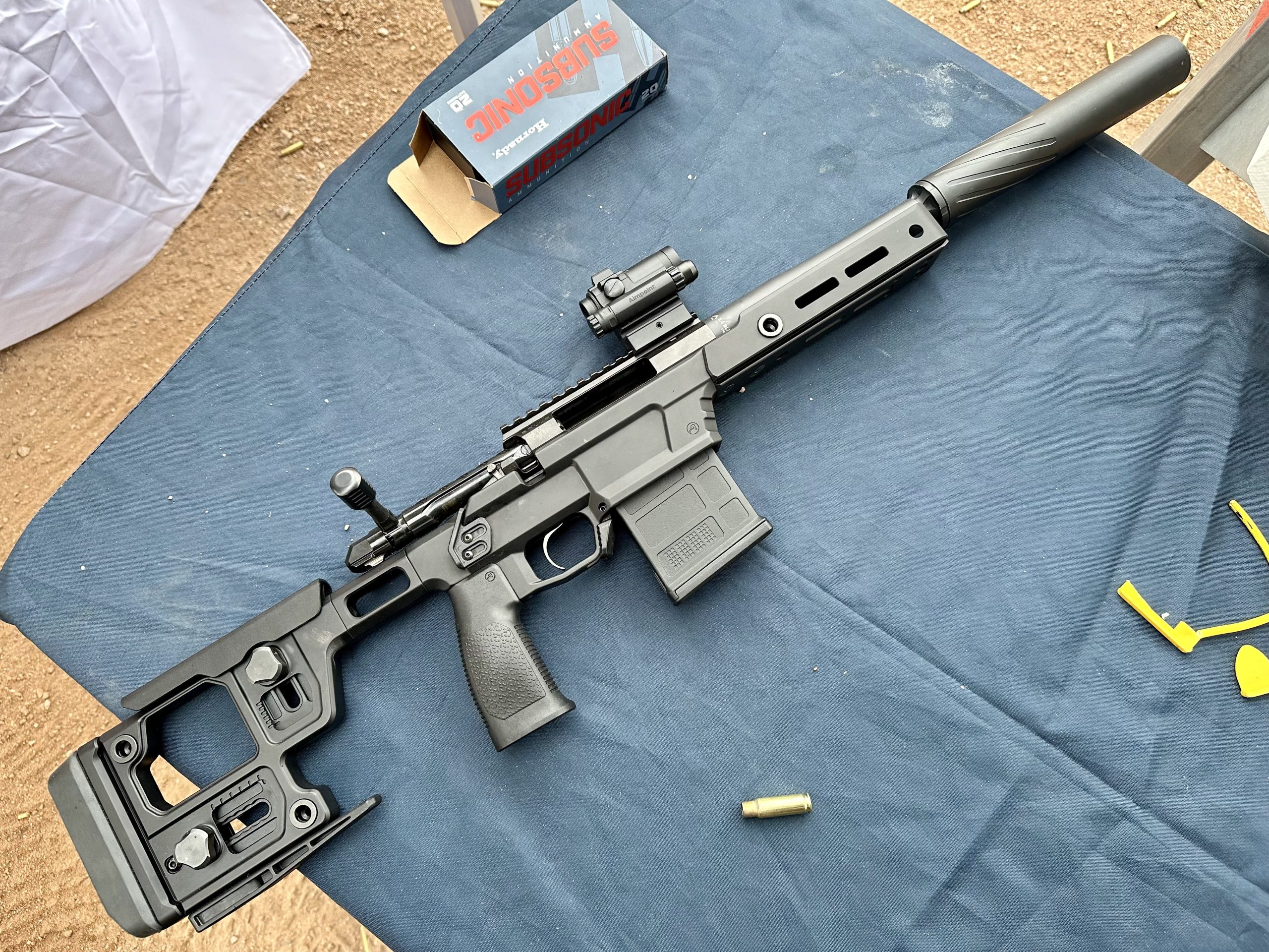 A black rifle lays posed on a blue table at the gun range.