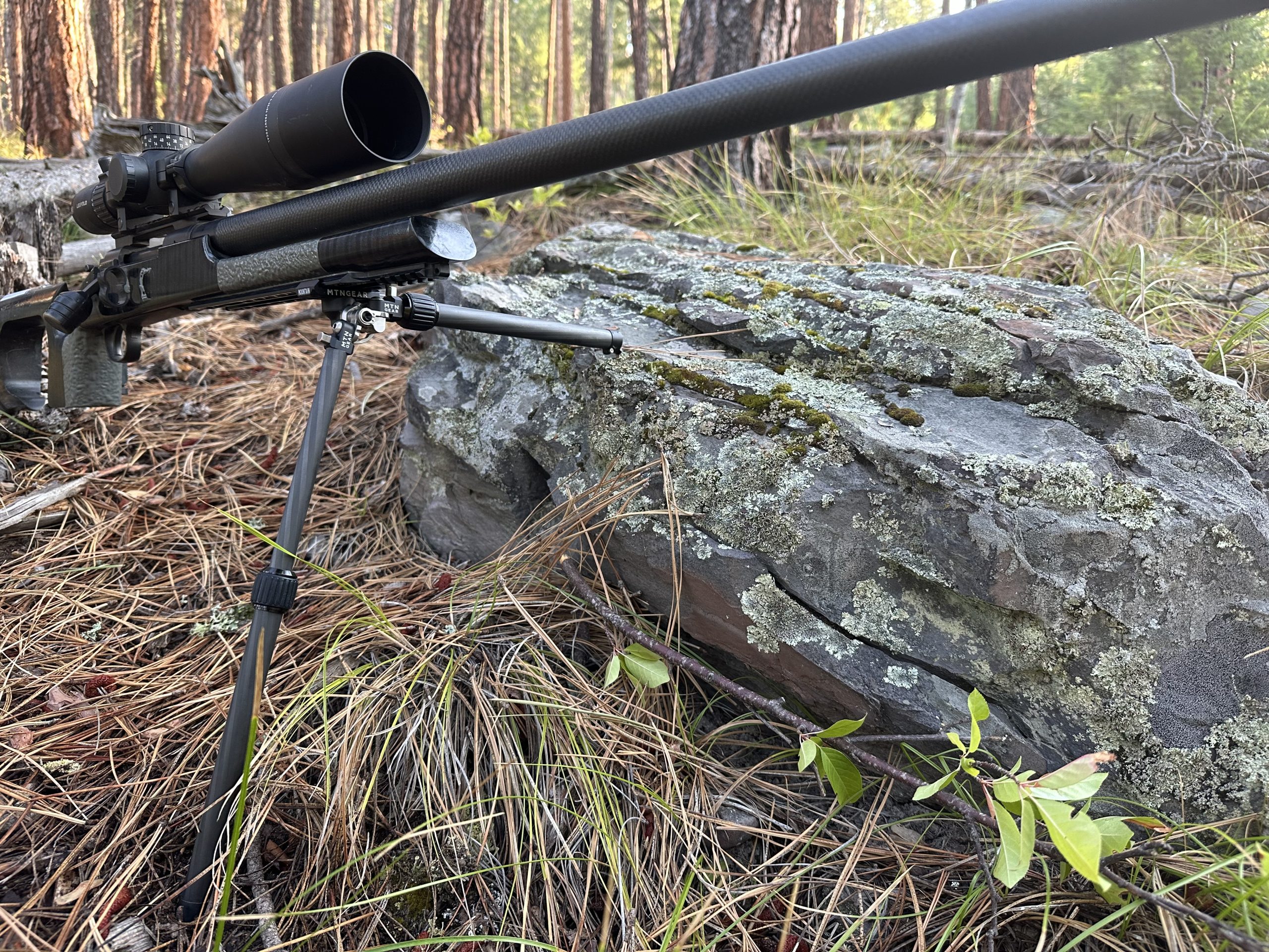 A rifle sits on a bipod in a rocky environment.