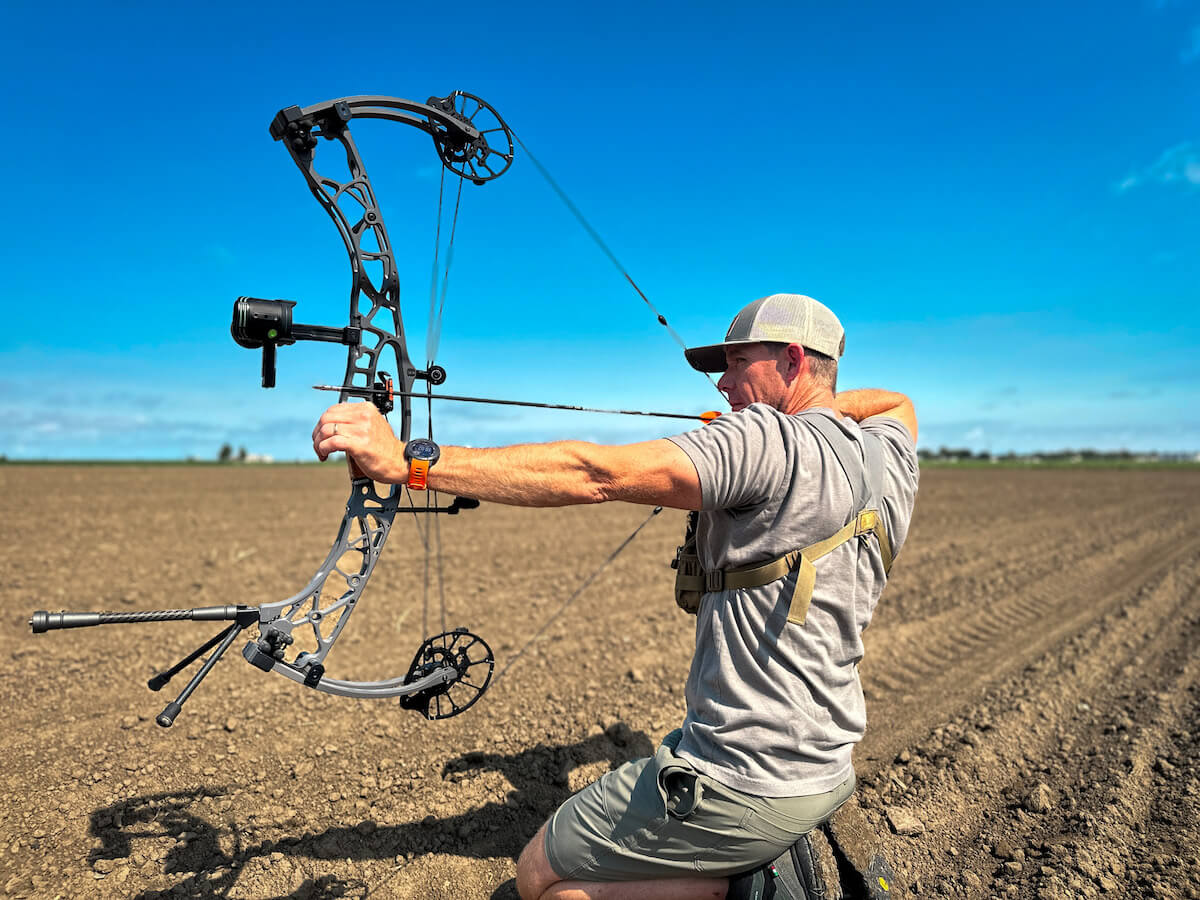 Man kneeling in field with bow and Ti 1.5 arrow tips