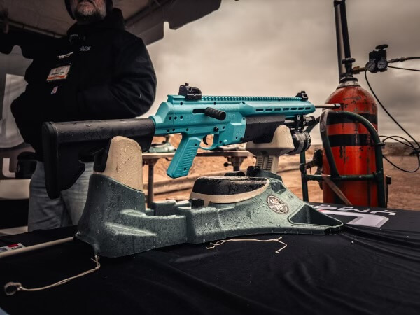 A blue air rifle with a fishing reel attached to it is shown on display.