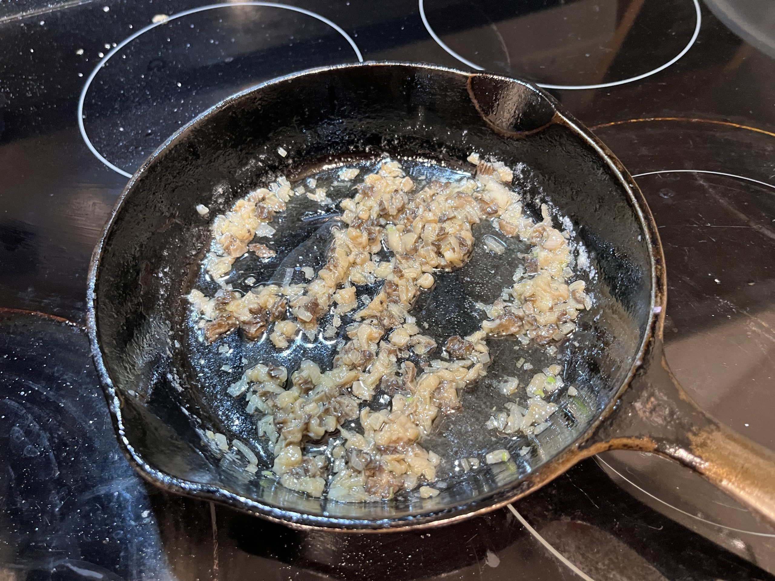 A cast iron pan with morel mushrooms cooking in butter