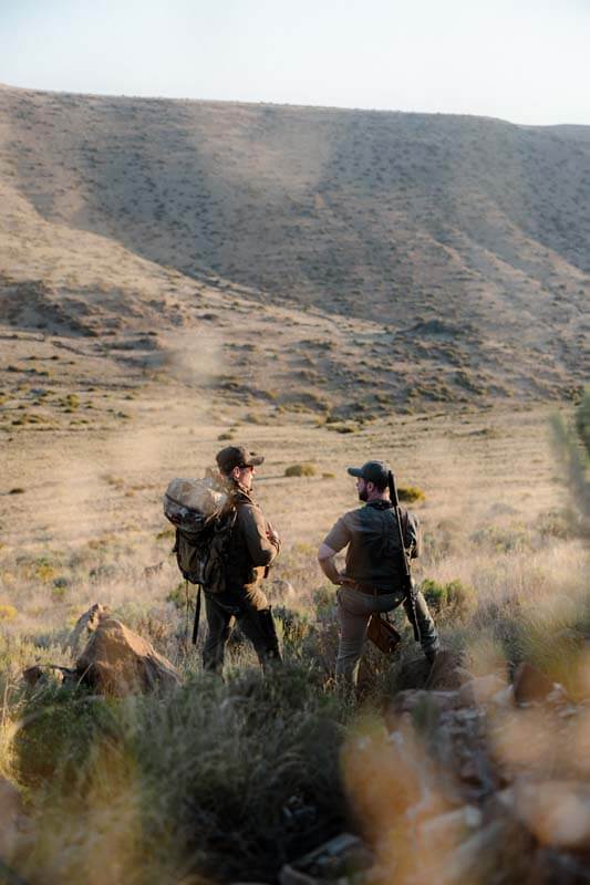 Two hunters standing in grass with gear and Dedito Luca boots