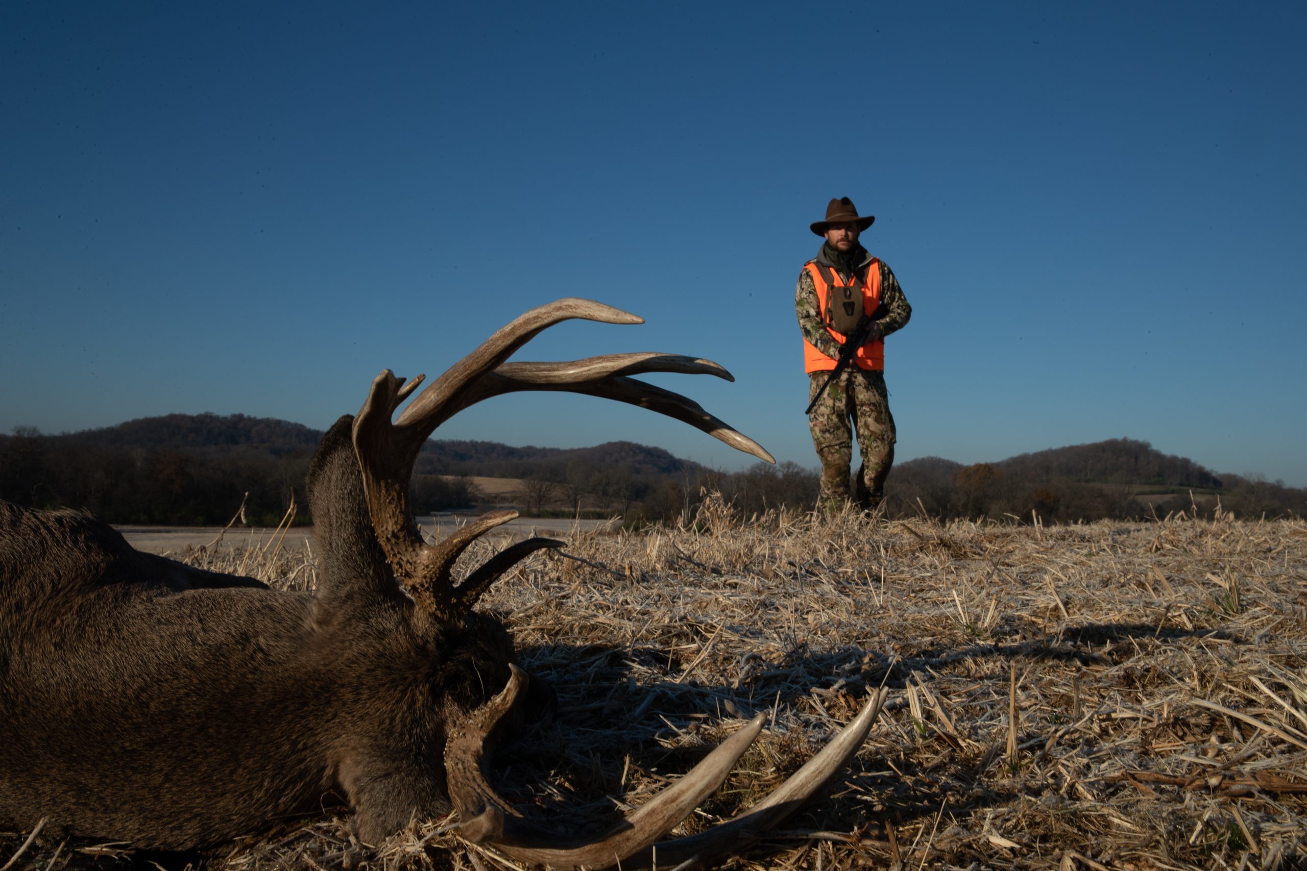 Hunter holding gun standing near a downed buck