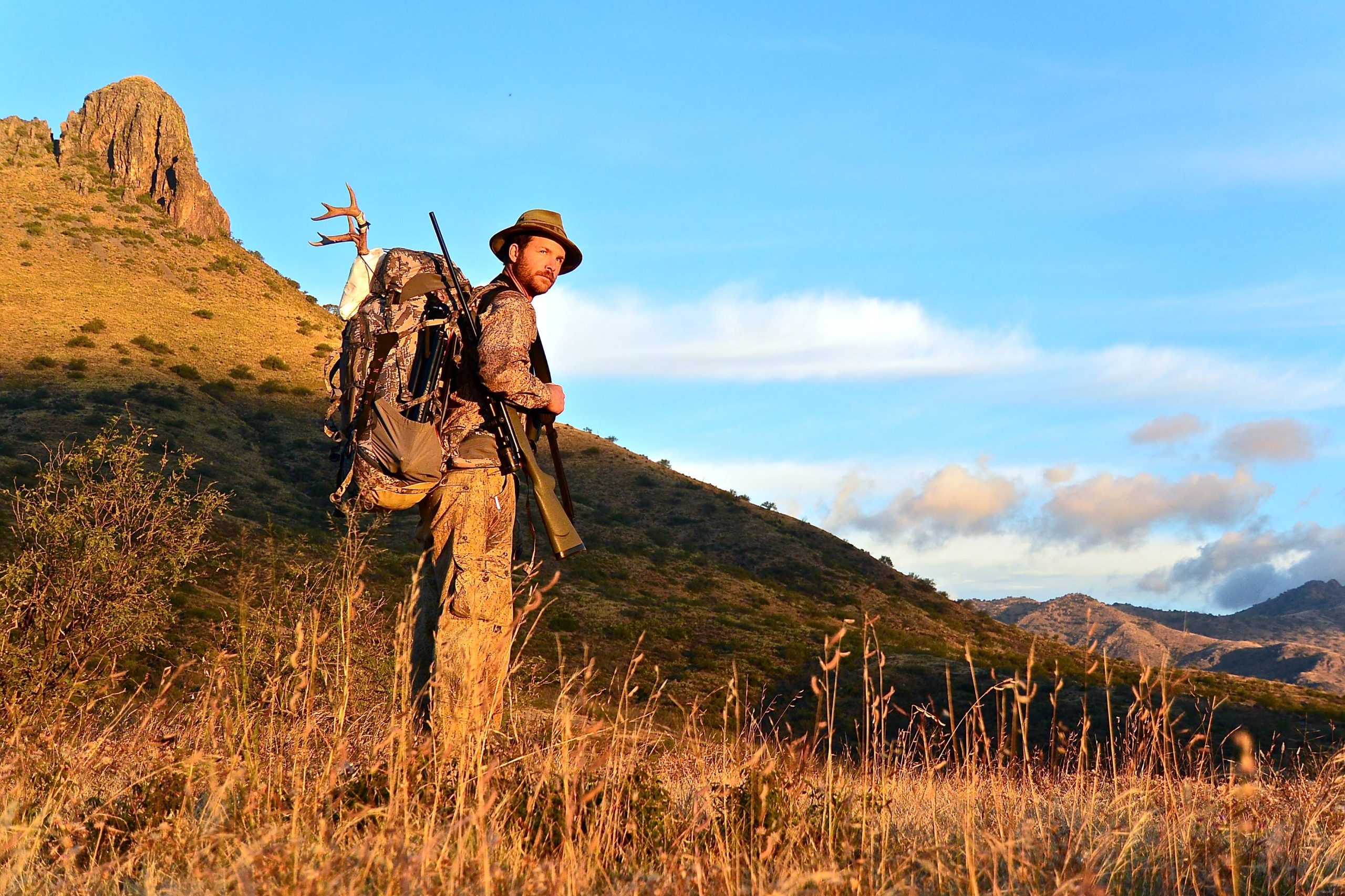 Hunter in the mountains with gun and coues deer