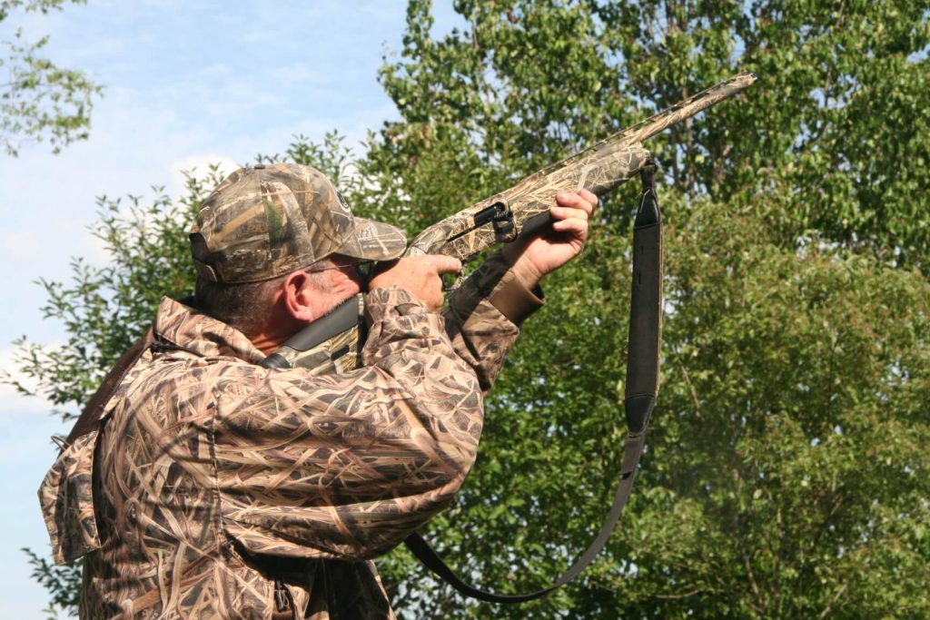 Hunter in camo aiming the Beretta A-400 at the trees above him