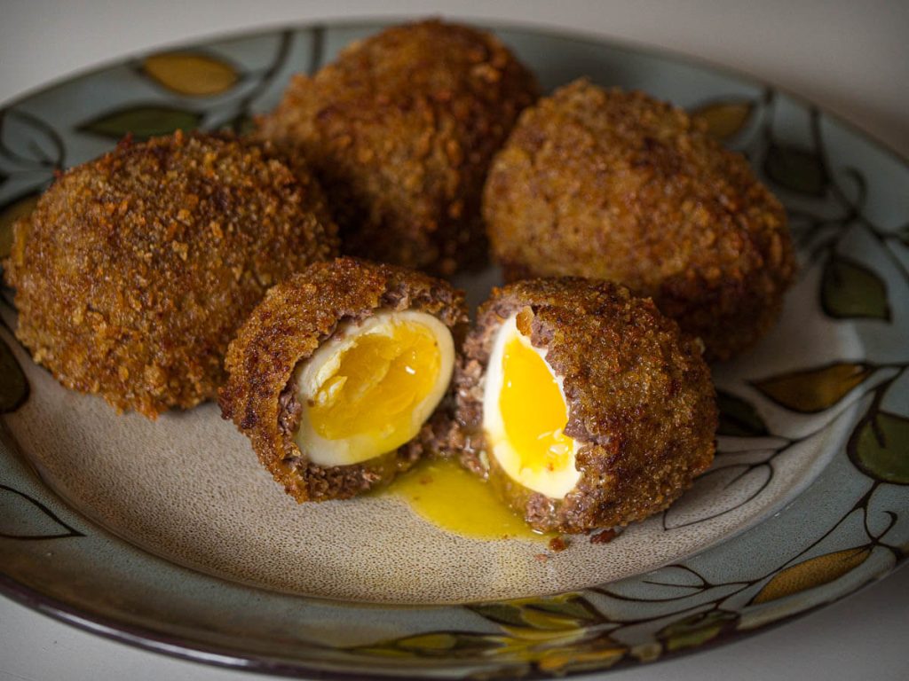 Scotch eggs on a plate, one cut open.