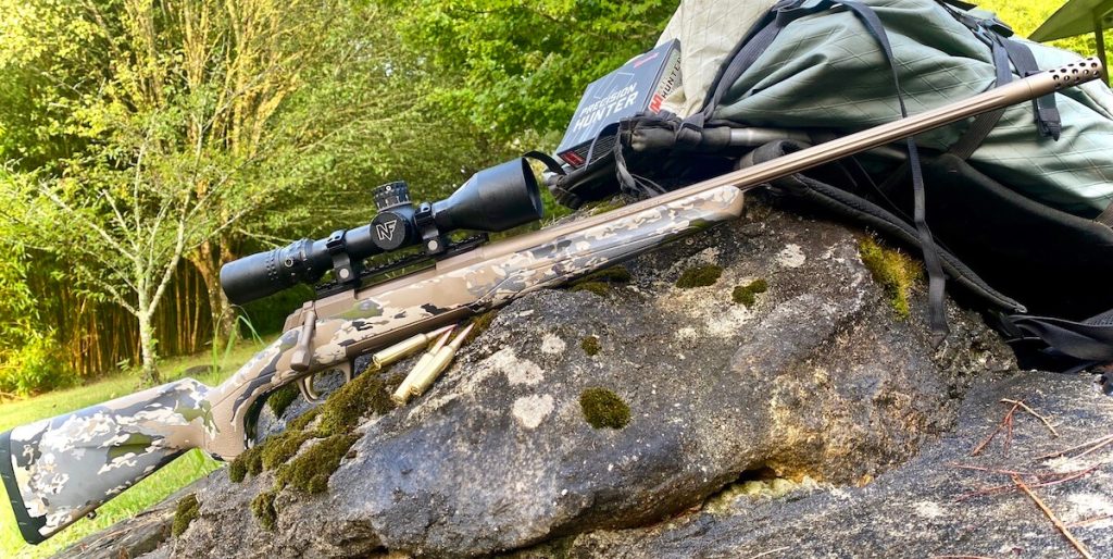 X-Bolt Speed SR with factory muzzle brake installed propped on large rocks with gear bag and ammmunition