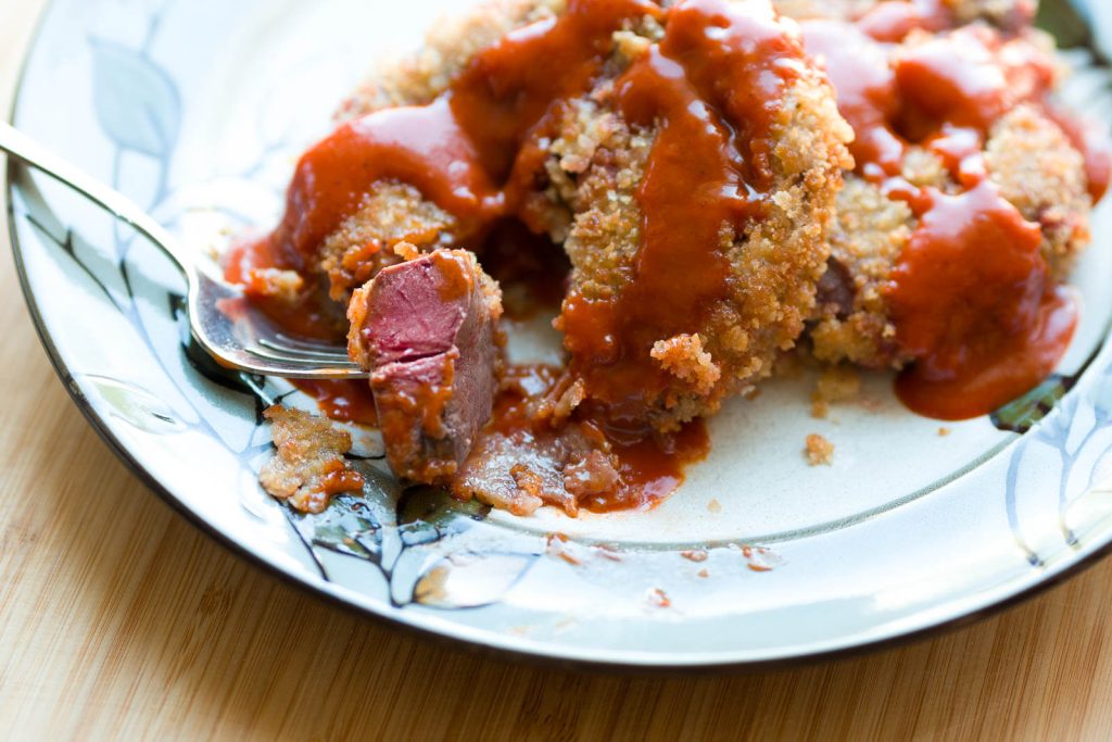 Fried elk heart with a red sauce on a china plate