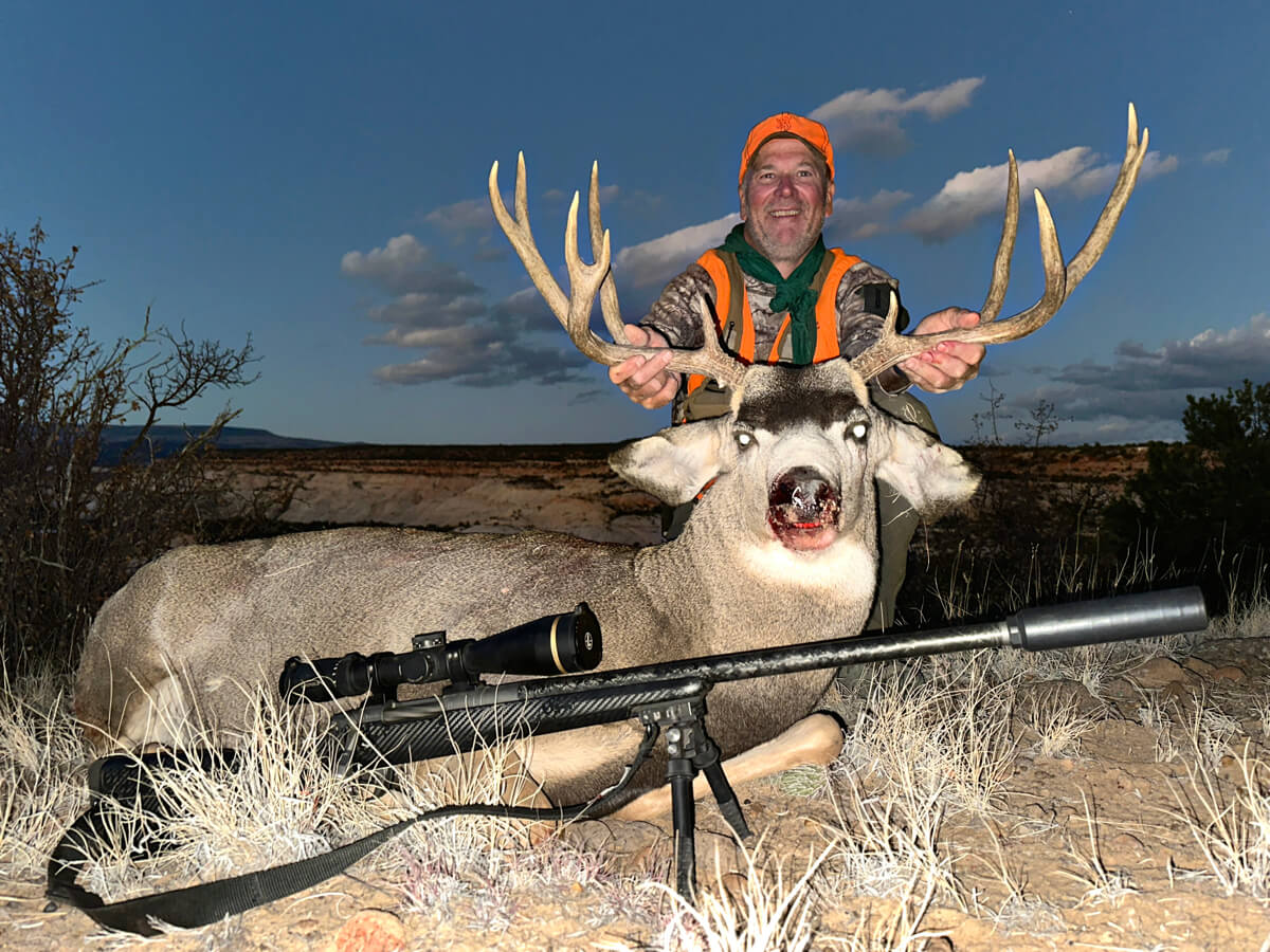 Gunwerks rifle posed in front of man with mule deer buck.