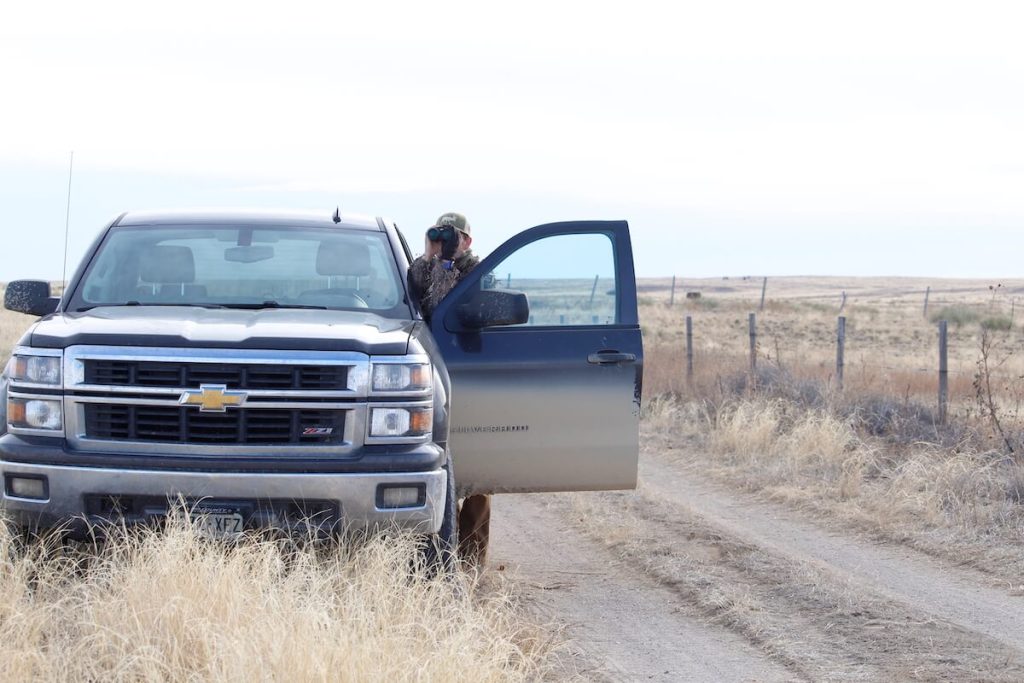 person standing by a truck with binoculars scouting for late season hunting