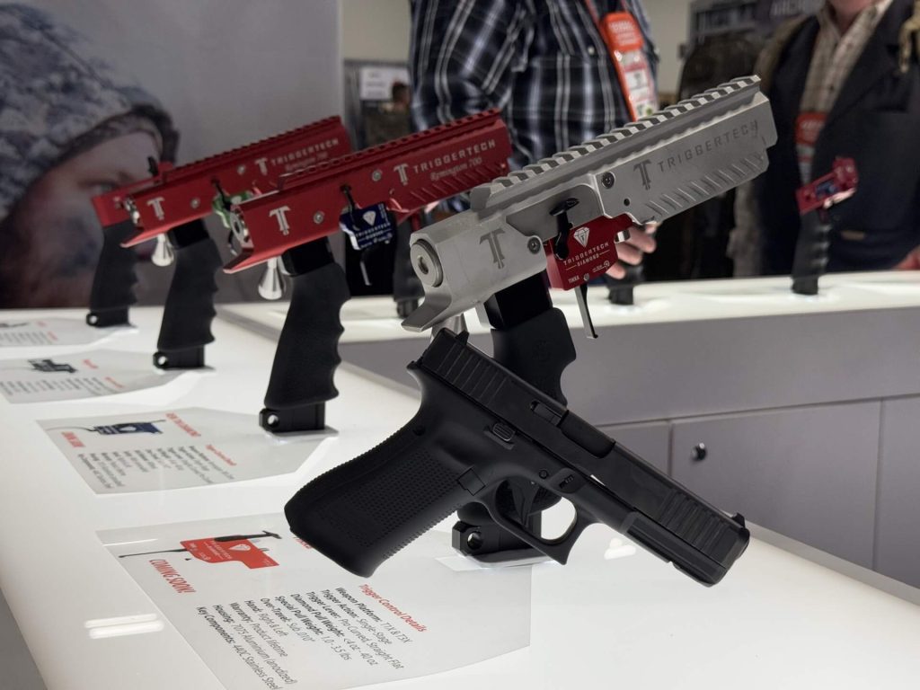 Multiple new trigger options from TriggerTech are on display at their booth during SHOT Show 2025. A pistol is up front, with four inert rifle models in the background, sporing TriggerTech Triggers.